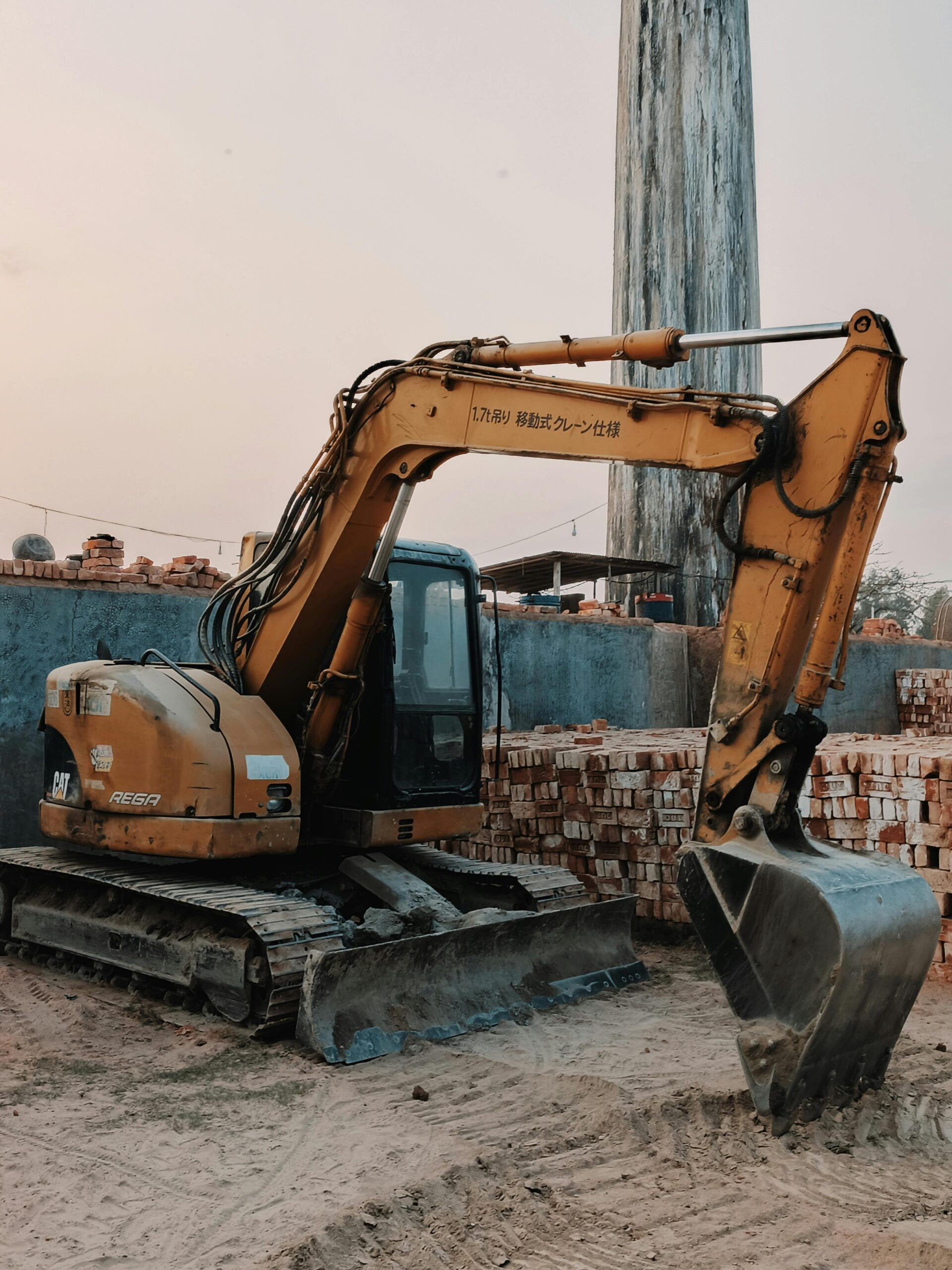Excavator at a construction site with building materials, captured at dusk.